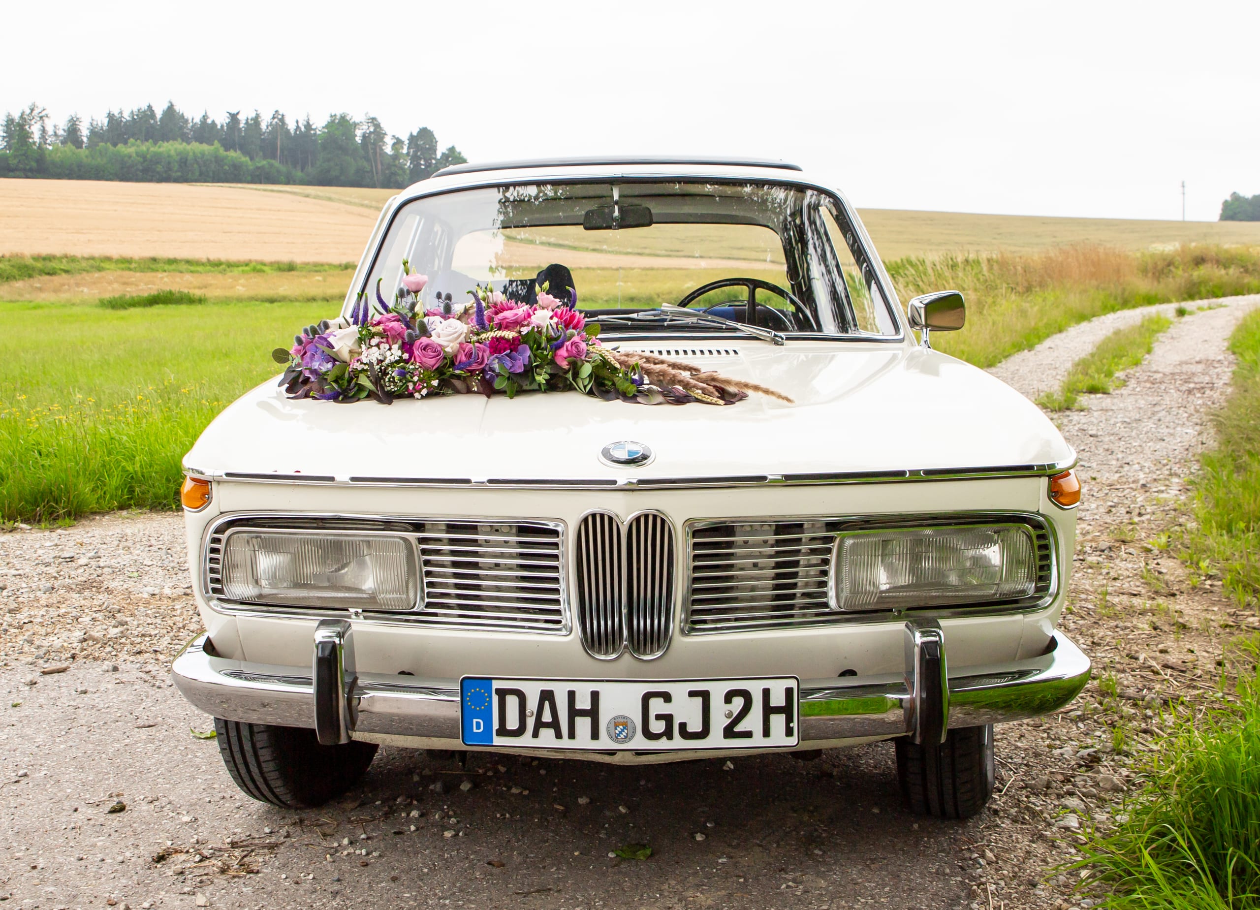 Weißer BMW-Oldtimer mit Brautstrauß auf einem Feldweg in Bayern — Hochzeit Catering Gold